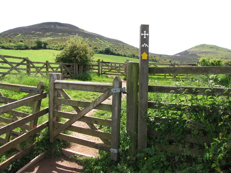 eildon hills en wegmarkering.jpg - De markering die we de komende dagen gaan volgen. Een kruis in de vorm van het kruis dat bij St Cuthbert is gevonden toen men in 1827 zijn kist heeft geopend voor onderzoek.Op de achtergrond de Eildon hills waar wij tussendoor moeten wandelen.